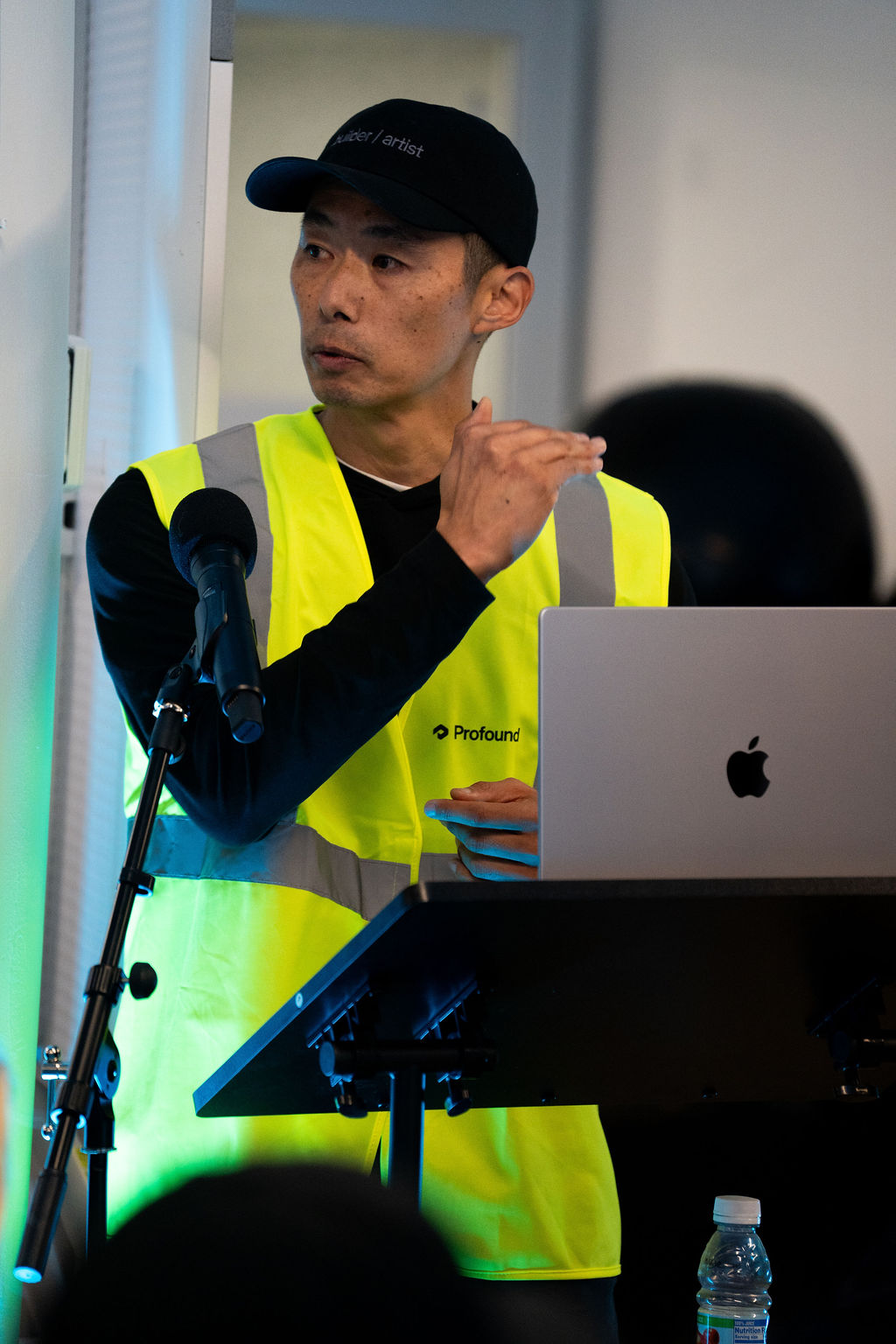 Gen pitching Flagship to the hackathon judges, in a Profound hi-vis vest at a podium